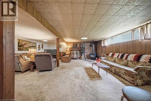 Spacious room featuring carpet flooring, wood paneling, a brick accent wall with a wood-burning stove, and overhead lighting - 1598 Highway No 6, Hamilton, ON - Indoor