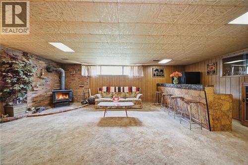 Finished lower level featuring a brick accent wall with a wood-burning stove, a built-in wet bar with stone-look detailing and a solid surface countertop, wood paneling, and a drop ceiling with integr - 1598 Highway No 6, Hamilton, ON - Indoor With Fireplace
