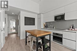 Modern kitchen featuring light wood-finish flooring, white flat-panel cabinetry, gray subway tile backsplash, stainless steel appliances, and a butcher block island - 