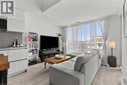 Open-concept living space featuring wood-finish flooring, a full-height window, and light-toned walls - 