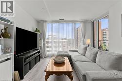 Living area featuring a large window with sheer drapes, light wood-finish flooring, and white walls - 