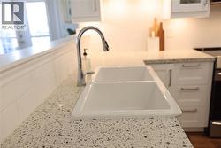 Kitchen featuring a double basin sink, chrome pull-down faucet, speckled light-toned countertop, white shaker-style cabinetry, and white subway tile backsplash - 