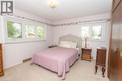 Carpeted interior space featuring multiple windows with blinds, a light-colored headboard, and a ceiling-mounted light fixture - 
