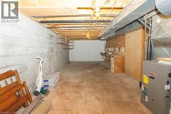 Unfinished basement featuring concrete block walls, exposed wooden joists, and a utility area with a built-in workbench - 