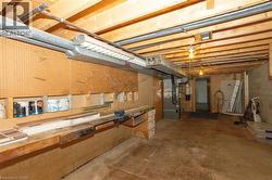 Basement workshop space featuring a long wooden workbench, pegboard wall, exposed ceiling beams, and concrete flooring - 