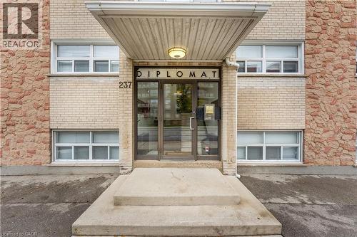 Building facade featuring a prominent main entrance, light brick exterior, and decorative stone accents - 237 Mohawk Road E Unit# 16, Hamilton, ON - Outdoor