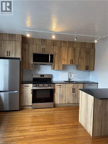Modern kitchen featuring wood-finish cabinetry, stainless steel appliances, black countertops, and a white tile backsplash - 237 Mohawk Road E Unit# 16, Hamilton, ON - Indoor Photo Showing Kitchen