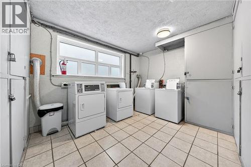 Utility area featuring multiple washers and dryers, white tiled flooring, a high window, and individual storage lockers - 237 Mohawk Road E Unit# 16, Hamilton, ON - Indoor Photo Showing Laundry Room
