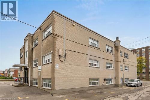 Three-story brick building featuring multiple windows and a paved parking area - 237 Mohawk Road E Unit# 16, Hamilton, ON - Outdoor With Exterior