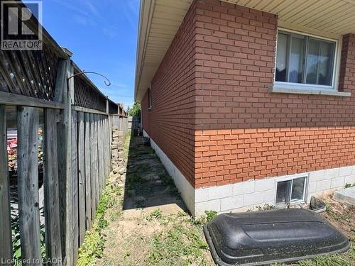Brick exterior with a white window frame, a window well, and a wood fence - 90 Anna Capri Drive Unit# Lower, Hamilton, ON - Outdoor With Exterior