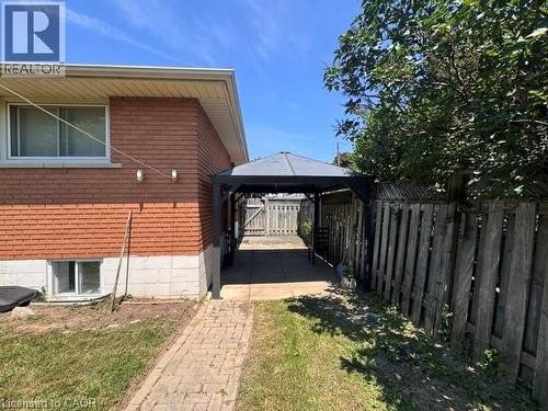 Exterior of the property featuring brick and block construction, a ground-level window, and a paved walkway leading to a covered patio area - 90 Anna Capri Drive Unit# Lower, Hamilton, ON - Outdoor With Exterior
