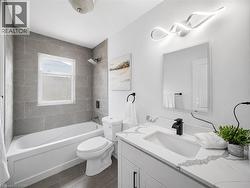Contemporary bathroom featuring a white soaking tub with gray tile surround, a single vanity with a white countertop, and a modern wall-mounted light fixture - 