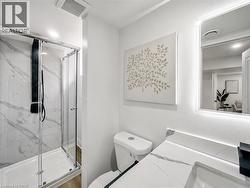 Bathroom featuring a glass-enclosed shower with black fixtures and marbled wall panels, a toilet, a vanity with a white countertop and integrated sink, and an illuminated mirror - 