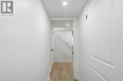Hallway with light wood-finish flooring, white baseboards, and bright recessed lighting - 