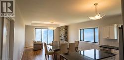 Open-concept living space featuring wood-finish flooring, a stone accent wall, and a tray ceiling with recessed lighting - 