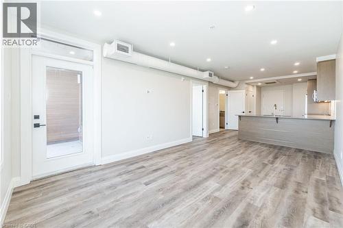 Expansive open-concept living area featuring wood-finish flooring, recessed lighting, a modern kitchen island with an undermount sink, contemporary cabinetry, and a glass-paneled exterior door - 72 Erb Street E Unit# 102, Waterloo, ON - Indoor Photo Showing Other Room