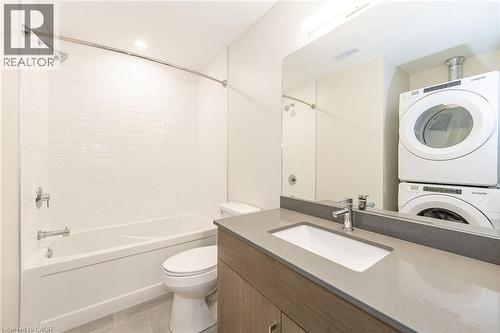 Bathroom featuring a tub/shower combination with white subway tile surround, a built-in vanity with a light gray countertop, and a stacked washer and dryer - 72 Erb Street E Unit# 102, Waterloo, ON - Indoor Photo Showing Laundry Room