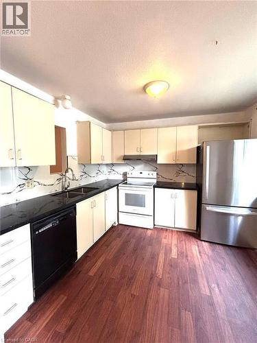 Kitchen featuring wood-finish flooring, cream cabinetry, dark countertops, and a patterned backsplash - 490 Third Street Unit# 40, London, ON - Indoor Photo Showing Kitchen With Double Sink