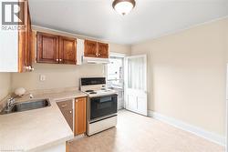 Kitchen featuring wood-finish cabinetry, solid surface countertops, a stainless steel sink, and a white electric range with an overhead ventilation hood - 
