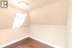Attic room featuring a sloped ceiling, an angled window, and wood-finish flooring - 