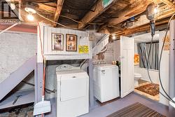 Laundry area featuring a side-by-side washer and dryer, exposed ceiling joists, and a partial view of a bathroom with a tub and toilet - 
