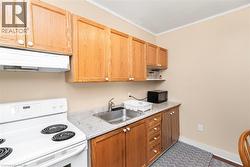 Compact kitchen featuring wood cabinetry, a white electric range with overhead exhaust, a stainless steel sink, and light-toned countertops - 
