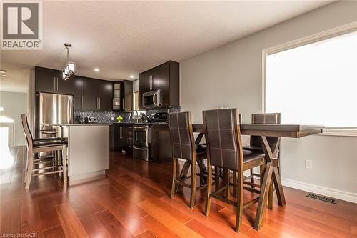 Modern kitchen featuring dark wood-finish cabinetry, stainless steel appliances, a mosaic tile backsplash, and a central island with an integrated breakfast bar - 44 Lemon Grass Street, Kitchener, ON - Indoor
