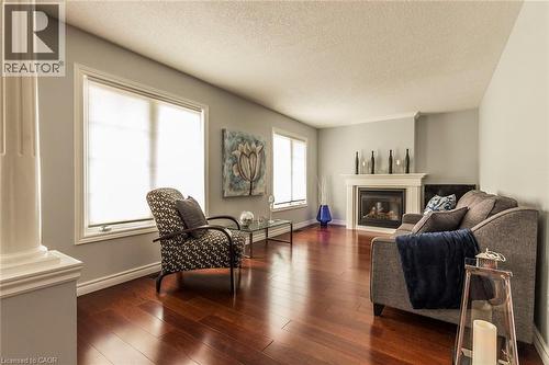 Living area featuring rich wood-finish flooring, a white mantel fireplace, and multiple windows with white trim - 44 Lemon Grass Street, Kitchener, ON - Indoor Photo Showing Living Room With Fireplace