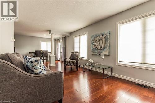 Expansive living area featuring rich wood-finish flooring, multiple windows with roller shades, and a structural column - 44 Lemon Grass Street, Kitchener, ON - Indoor