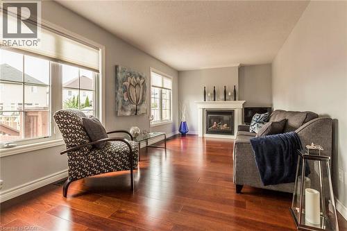 Living area featuring rich wood-finish flooring, light gray wall tones, a corner fireplace with a white mantel, and multiple windows - 44 Lemon Grass Street, Kitchener, ON - Indoor Photo Showing Living Room With Fireplace