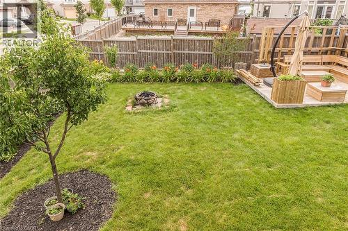 Expansive backyard featuring a lush lawn, established tree, and a built-in fire pit on a stone base - 44 Lemon Grass Street, Kitchener, ON - Outdoor