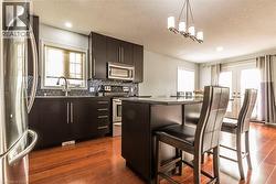 Kitchen featuring dark wood-finish cabinetry, stainless steel appliances, a tile backsplash, and a breakfast bar with seating - 