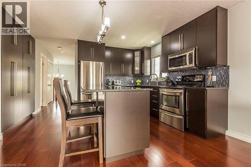 Kitchen featuring dark wood-finish cabinetry, stainless steel appliances, a tiled backsplash, wood-finish flooring, and a central island with bar seating - 44 Lemon Grass Street, Kitchener, ON - Indoor Photo Showing Kitchen With Stainless Steel Kitchen