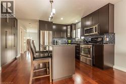 Kitchen featuring dark wood-finish cabinetry, stainless steel appliances, a tiled backsplash, wood-finish flooring, and a central island with bar seating - 