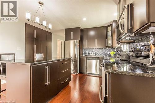 Modern kitchen featuring dark wood-finish cabinetry, stainless steel appliances, a center island with bar seating, and a mosaic tile backsplash - 44 Lemon Grass Street, Kitchener, ON - Indoor Photo Showing Kitchen With Stainless Steel Kitchen With Upgraded Kitchen