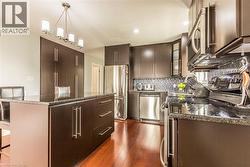 Modern kitchen featuring dark wood-finish cabinetry, stainless steel appliances, a center island with bar seating, and a mosaic tile backsplash - 