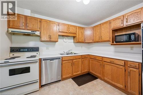 Kitchen featuring wood cabinetry, white countertops, a stainless steel dishwasher, a white electric range with a coordinating range hood, and tile flooring - 4 Albert Street Unit# 105, Cambridge, ON - Indoor Photo Showing Kitchen With Double Sink