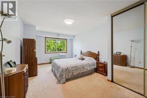 Carpeted bedroom with a window overlooking mature trees, featuring a ceiling-mounted light fixture and a full-height mirrored closet door - 4 Albert Street Unit# 105, Cambridge, ON - Indoor Photo Showing Bedroom