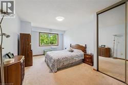 Carpeted bedroom with a window overlooking mature trees, featuring a ceiling-mounted light fixture and a full-height mirrored closet door - 