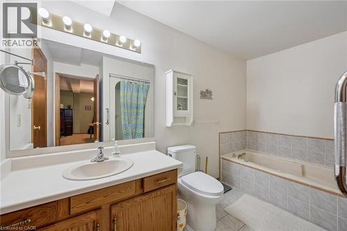 Bathroom featuring a single vanity with wood-finish cabinetry, a large wall-mounted mirror, a built-in bathtub with tiled surround, and a separate shower enclosure with a patterned curtain - 4 Albert Street Unit# 105, Cambridge, ON - Indoor Photo Showing Bathroom