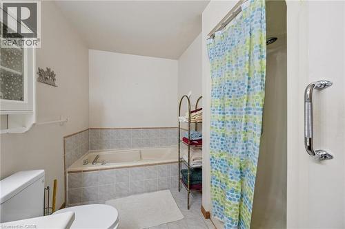 Bathroom featuring a built-in bathtub with tiled surround, a separate shower enclosure, and a wall-mounted storage cabinet with frosted glass panels - 4 Albert Street Unit# 105, Cambridge, ON - Indoor Photo Showing Bathroom