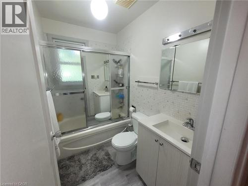 Bathroom featuring a full tub with sliding glass enclosure, mosaic tile wainscoting, vanity with integrated sink, and wood-finish flooring - 879 West 5Th Street, Hamilton, ON - Indoor Photo Showing Bathroom