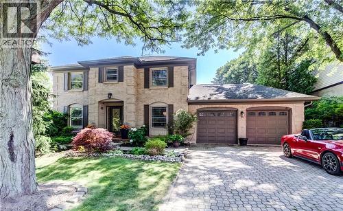 Two-story stone exterior residence featuring a two-car garage with arched entrances, a paver stone driveway, and mature landscaping - 41 Mcniven Road, Ancaster, ON - Outdoor