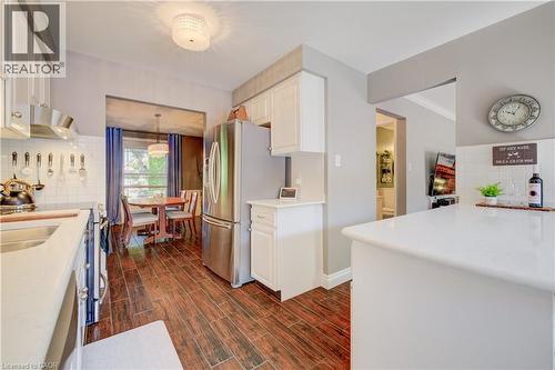 Kitchen featuring wood-finish flooring, white cabinetry, stainless steel appliances, white subway tile backsplash, and a breakfast bar with a solid surface countertop - 41 Mcniven Road, Ancaster, ON - Indoor Photo Showing Kitchen With Double Sink