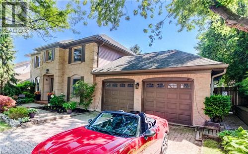 Traditional two-story residence featuring a stone and siding exterior, a double-door garage with paneled doors, a paver driveway, and established front landscaping - 41 Mcniven Road, Ancaster, ON - Outdoor