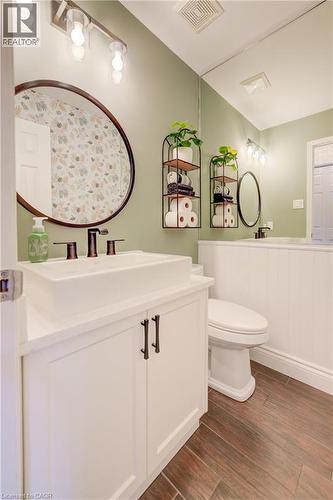 Bathroom featuring a vessel sink atop a white vanity with dark hardware, dark wood-finish flooring, and a round wall mirror with a dark frame - 41 Mcniven Road, Ancaster, ON - Indoor Photo Showing Bathroom