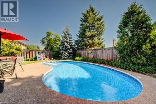 Kidney-shaped swimming pool featuring a textured concrete surround, metal pool steps, and a surrounding privacy fence - 41 Mcniven Road, Ancaster, ON - Outdoor With In Ground Pool With Backyard