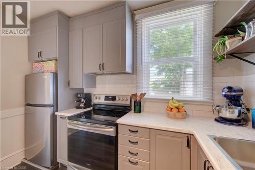 Kitchen featuring light gray cabinetry with black hardware, white subway tile backsplash, light-toned countertops, and a window with white blinds - 39 Kerr Street, Cambridge, ON - Indoor Photo Showing Kitchen