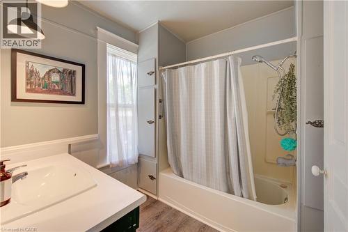 Bathroom featuring a shower-over-tub combination, a single vanity with a white countertop and integrated sink, a window with sheer curtains, built-in storage cabinetry, and wood-finish flooring - 39 Kerr Street, Cambridge, ON - Indoor Photo Showing Bathroom