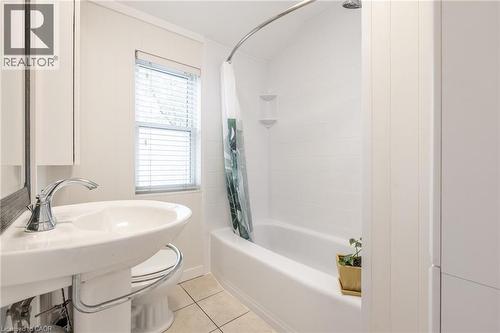 Bathroom featuring a white pedestal sink with chrome faucet, a white bathtub with a tiled surround, and a window with horizontal blinds - 851 Beach Boulevard, Hamilton, ON - Indoor Photo Showing Bathroom